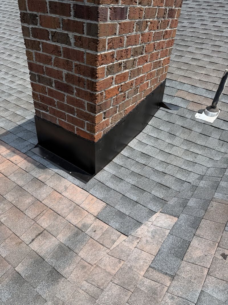 New dark flashing at the base of a brick chimney on a shingle roof