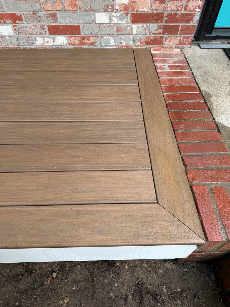 Corner of a deck surface with border boards framing the deck boards beside brick steps
