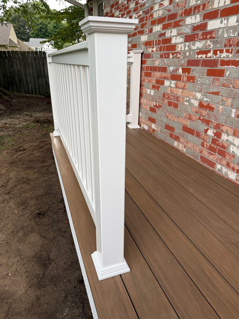 White railing post and balusters along the edge of a deck next to a brick wall