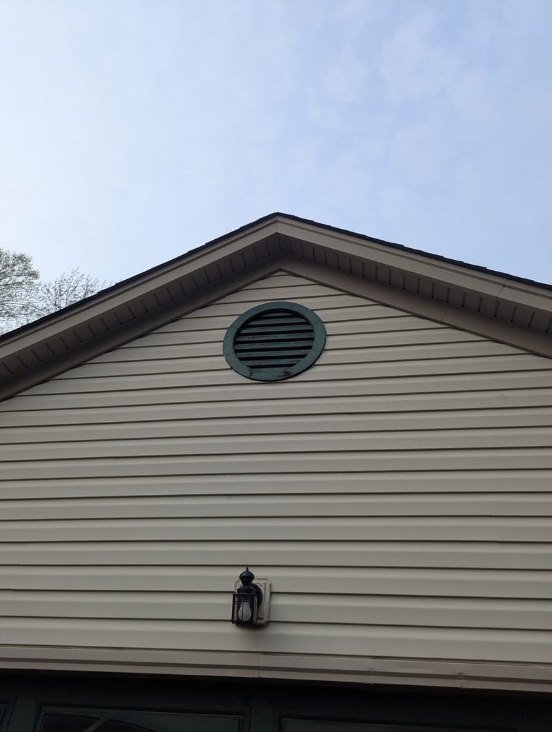 Beige vinyl-sided garage gable with round green vent, light fixture and green garage door