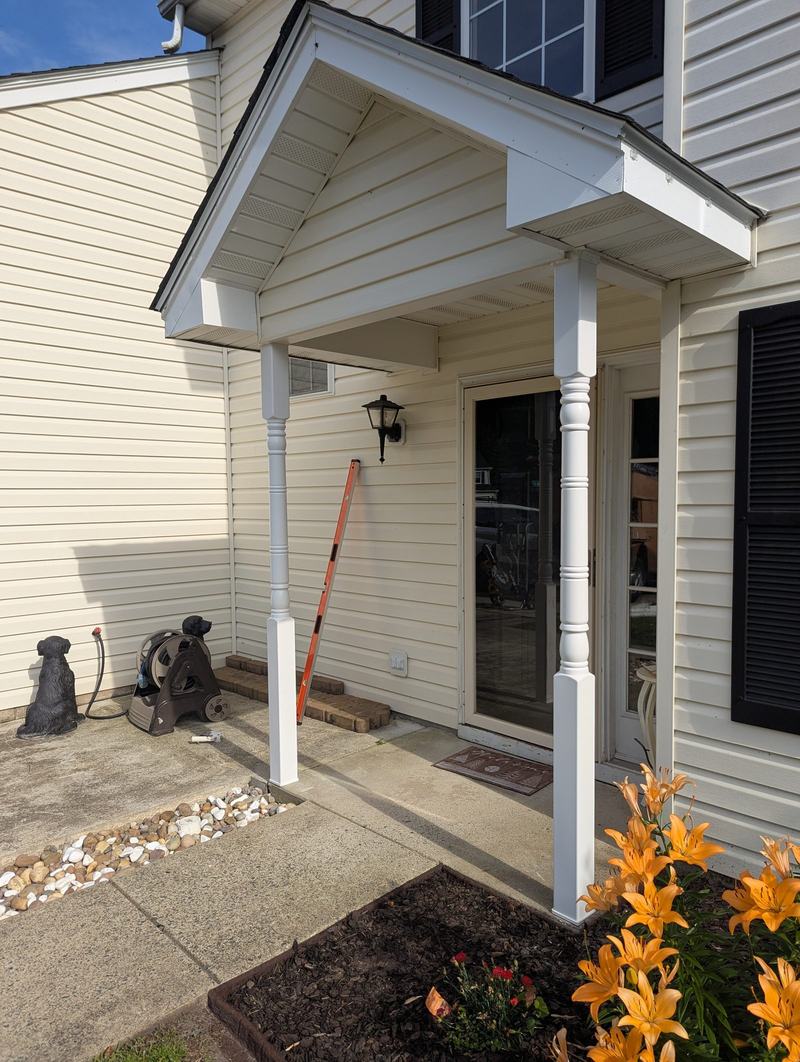 Covered front entry with two white turned porch columns, orange lilies in the foreground