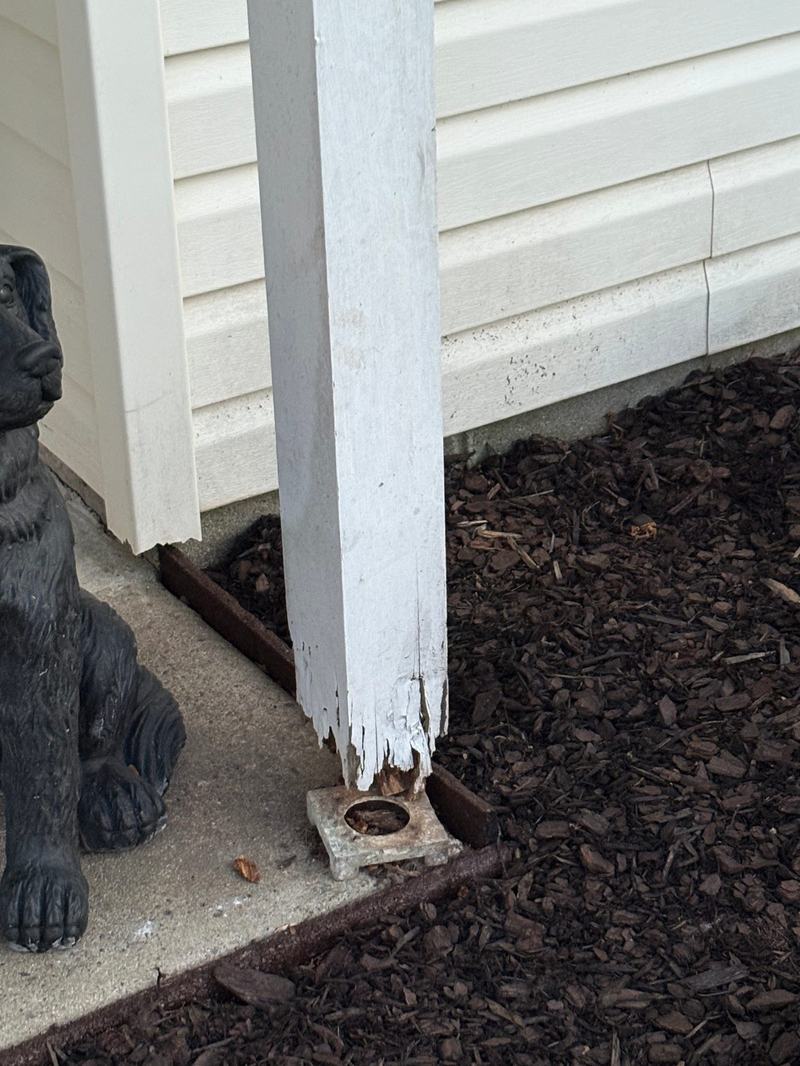 Close-up of a white wooden porch post with a rotted, splitting base on concrete
