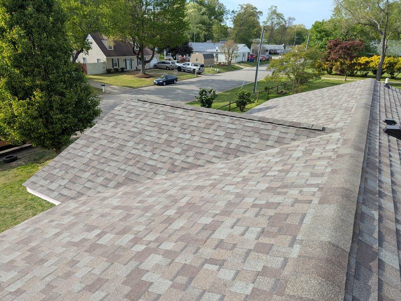 Newly shingled roof with tan and brown architectural shingles meeting at a valley under a clear sky